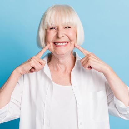 Woman smiling and pointing to her dental implants on blue background