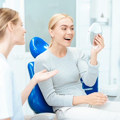 Woman admiring the results of her cosmetic dental procedure in mirror