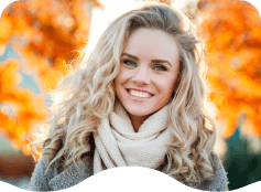 Blonde woman in scarf smiling with autumn trees in background