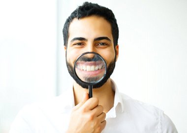 man holding magnifying glass to his smile with dental crowns in Granby 