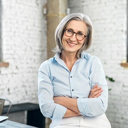 Senior woman with glasses smiling with her arms folded