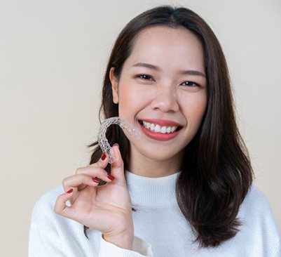 smiling woman holding an Invisalign aligner 