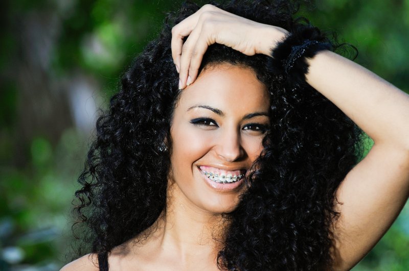 a young woman standing outside and smiling wide as she shows off her traditional braces