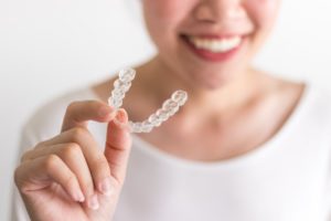 person smiling while holding an Invisalign aligner 