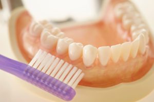 Purple toothbrush held up to a set of dentures